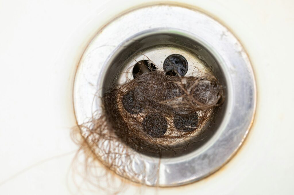 Close-up. Bathroom drain is clogged with dark human hair. Sanitation and hygiene. Stress and illness